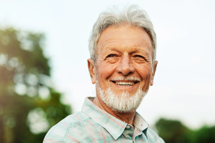 Smiling older man with gray hair outdoors in casual shirt, dental care professional portrait.