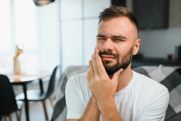 Man touching his cheek in discomfort in a modern dental office setting.
