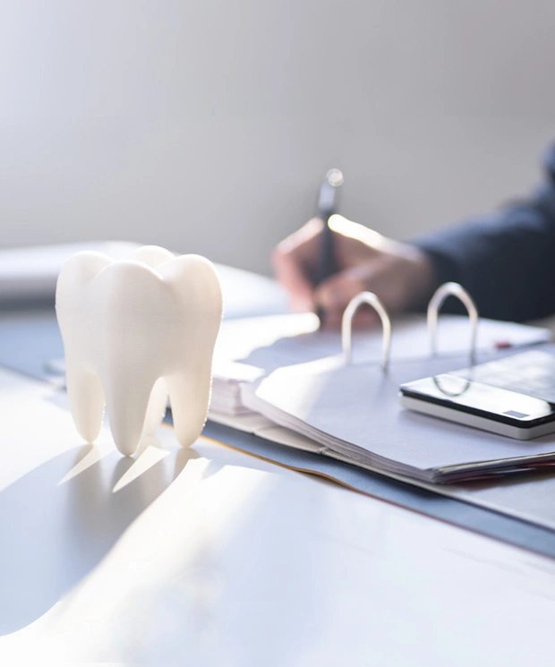 White tooth model on dental office desk with dentist writing notes in background
