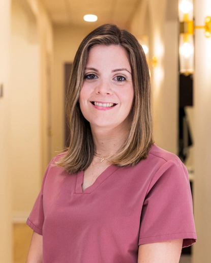 Woman in pink scrubs smiling in dental office hallway