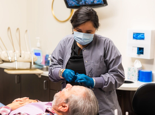 Dentist in mask and gloves examining elderly patient in dental office treatment room.