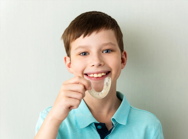 Young boy in turquoise shirt smiling while holding dental floss against white background.