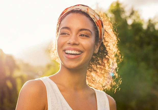 Smiling woman wearing headband outdoors in sunny park setting during golden hour