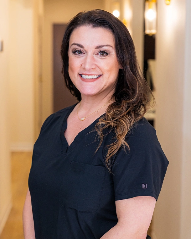 Dental care professional in scrubs smiling in modern office hallway at Bethany Heights Dental Care.