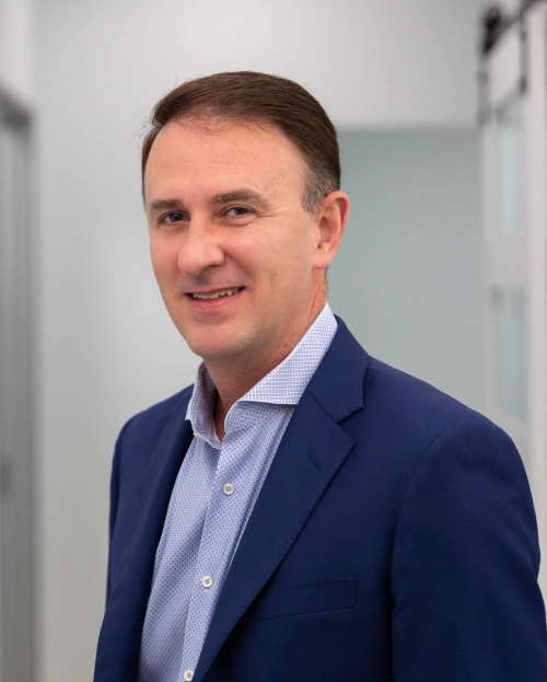 Professional headshot of male dental care provider in blue blazer and light blue shirt, indoor office setting.