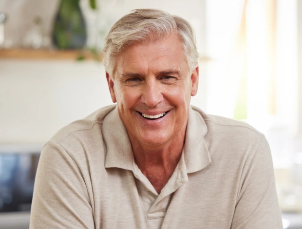 Smiling mature man in casual beige shirt, dental care professional or patient in bright indoor setting.