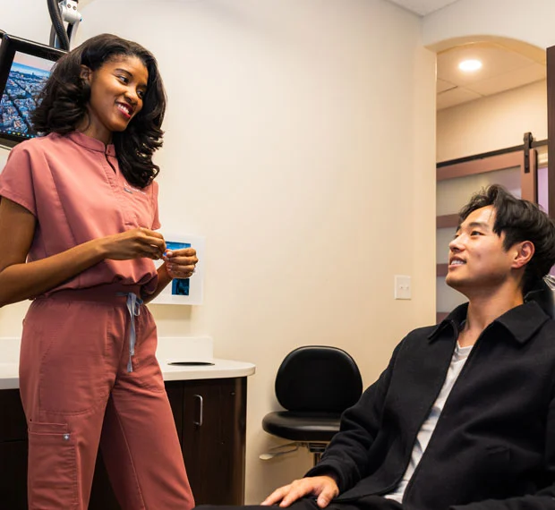 Female dentist in pink scrubs consulting with male patient in dental office setting.