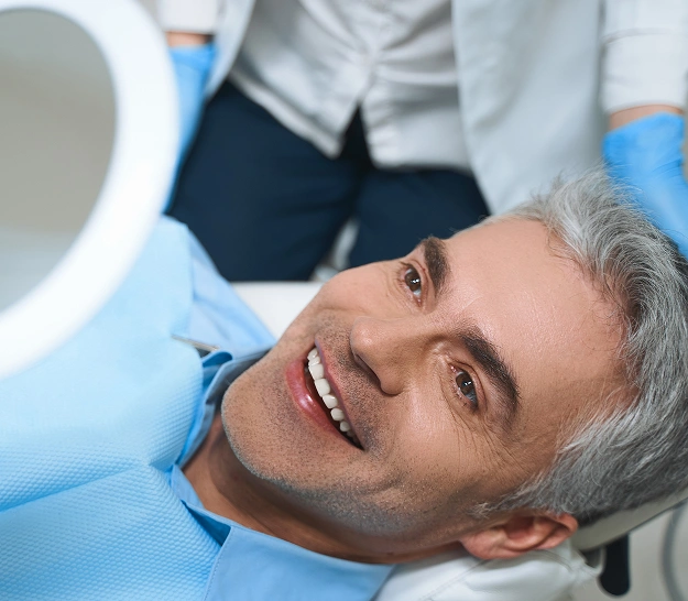 Male patient smiling during dental examination in bright clinical treatment room at dentist office.